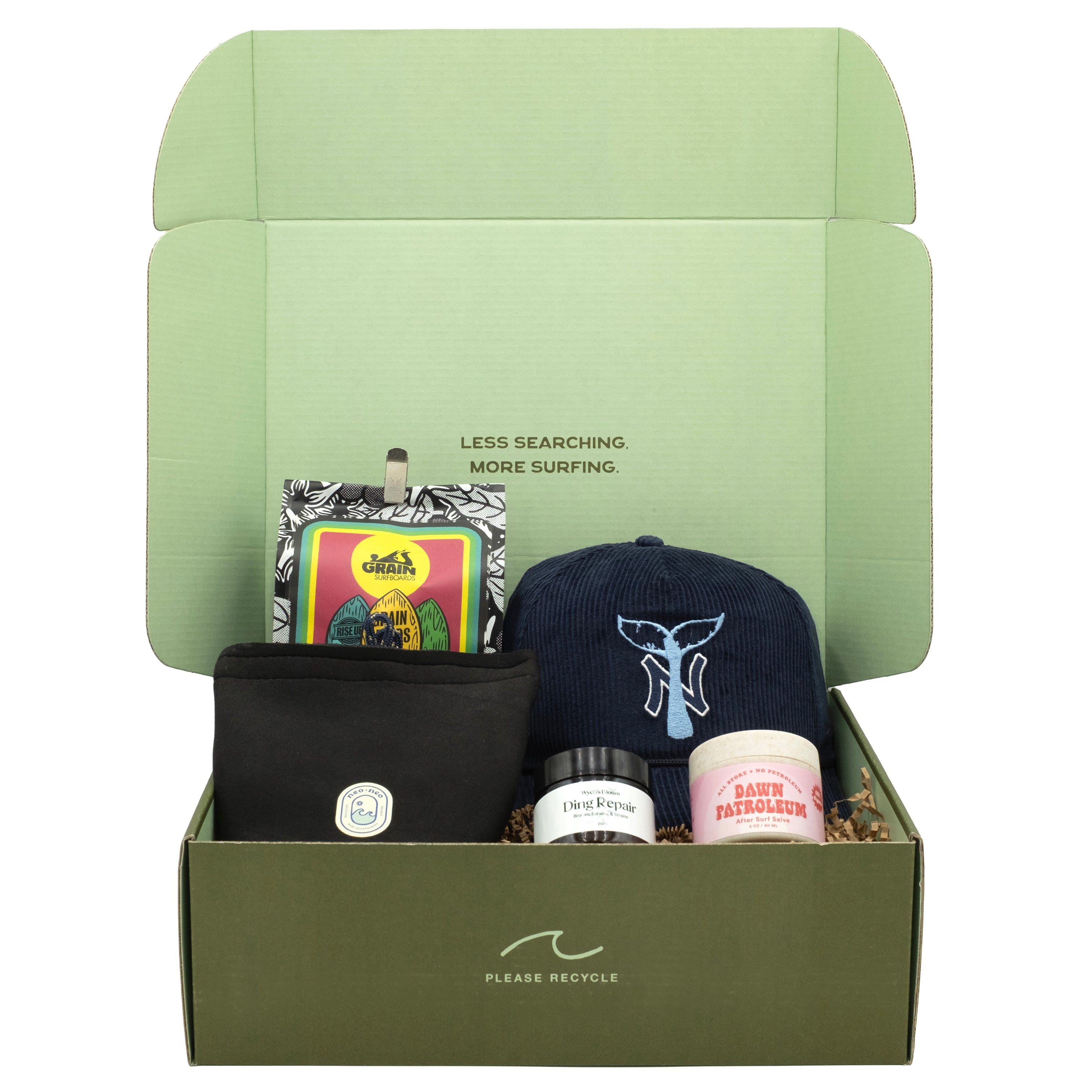 A curated surf-themed gift box set by The Nami Box, featuring a sage green cardboard box with an open lid, containing a navy blue whale tail baseball cap, a black pouch, a small jar, and a pink tin, all arranged on a white background.